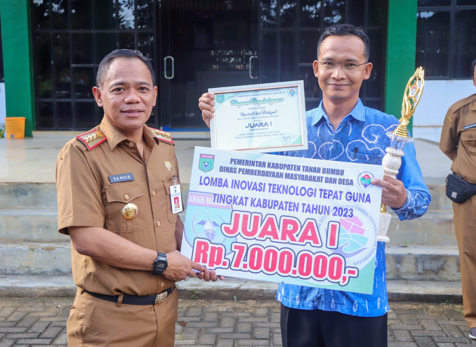 Kepala Dinas Pemberdayaan Masyarakat dan Desa Kabupaten Tanah Bumbu Samsir menyerahkan Reward pemenang Lomba Inovasi Tepat Guna Tingkat Kabupaten, di halaman kantor dinas setempat, Selasa (13/6/2023). (Kalimantanlive.com/ Desy)
